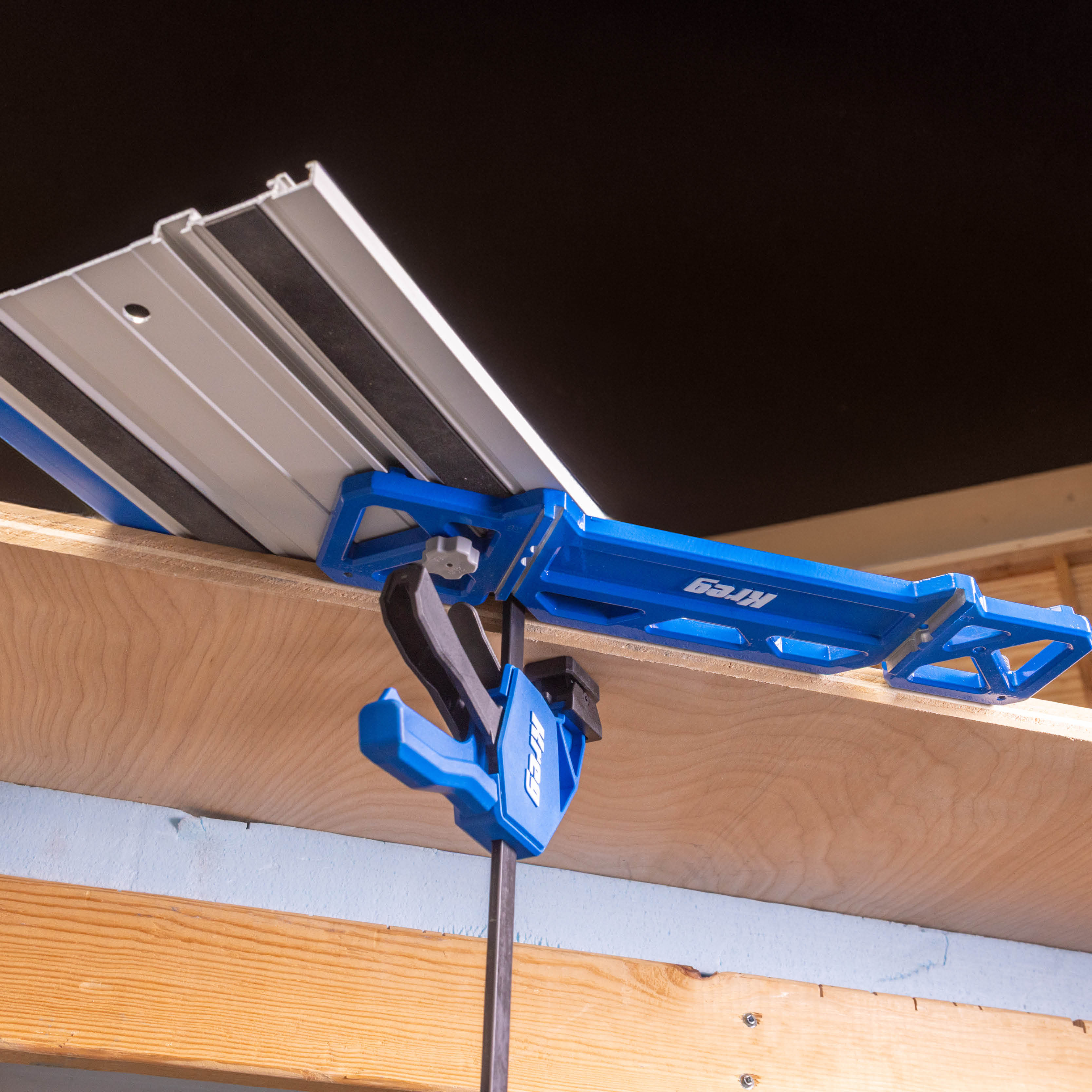 A view of the underside of a sheet of plywood, with the Kreg Universal Track on top of it and the Kreg Track Square and Track Clamps used as accessories.