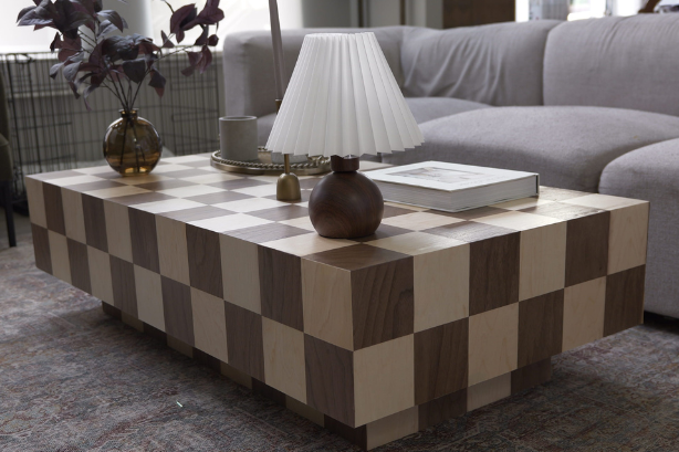 A checkered wooden coffee table with a lamp and accessories on top of it sits in a living room setting.