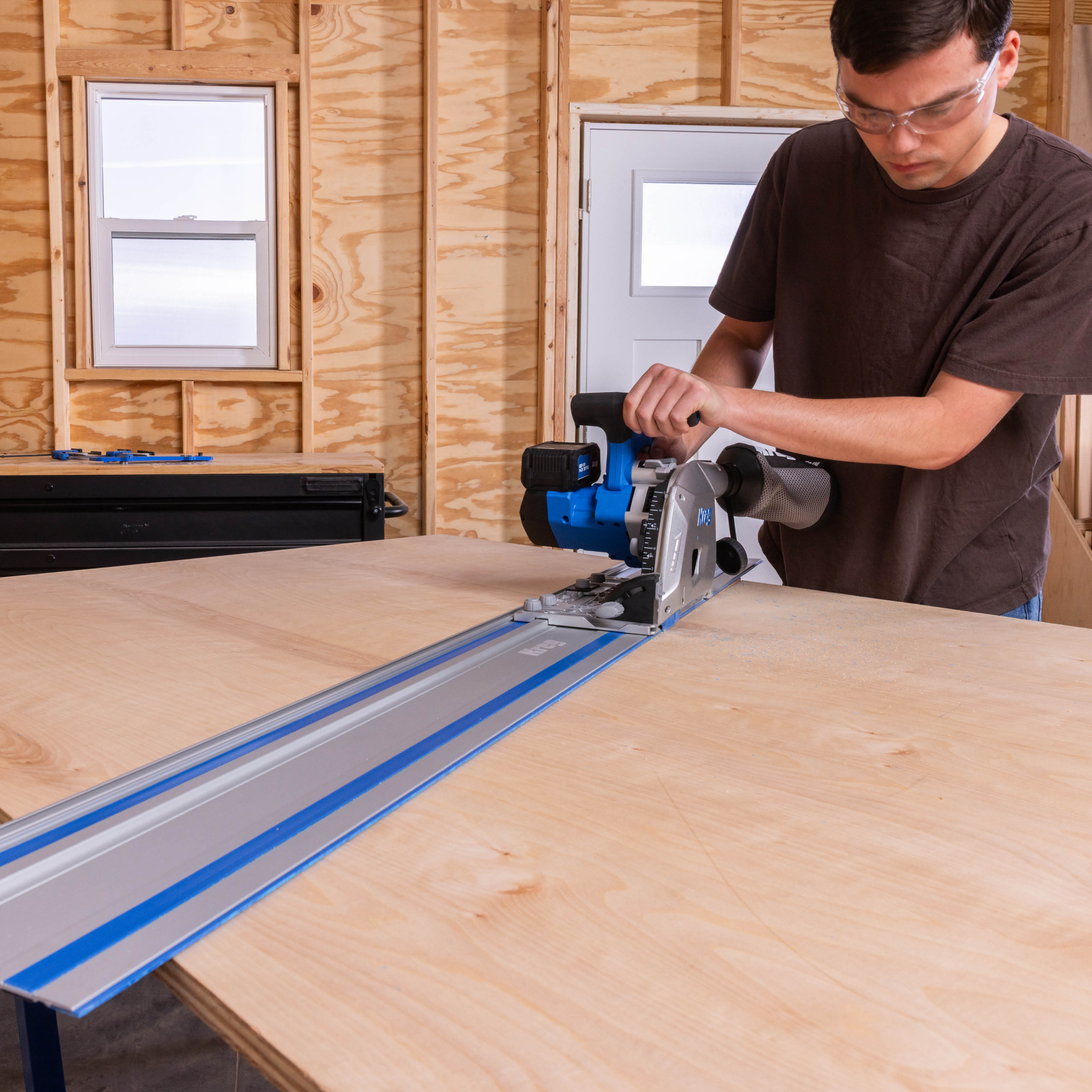A man concentrates on cutting an angled cut across a sheet of plywood using the Kreg Adaptive Cutting System Saw + Universal Track.