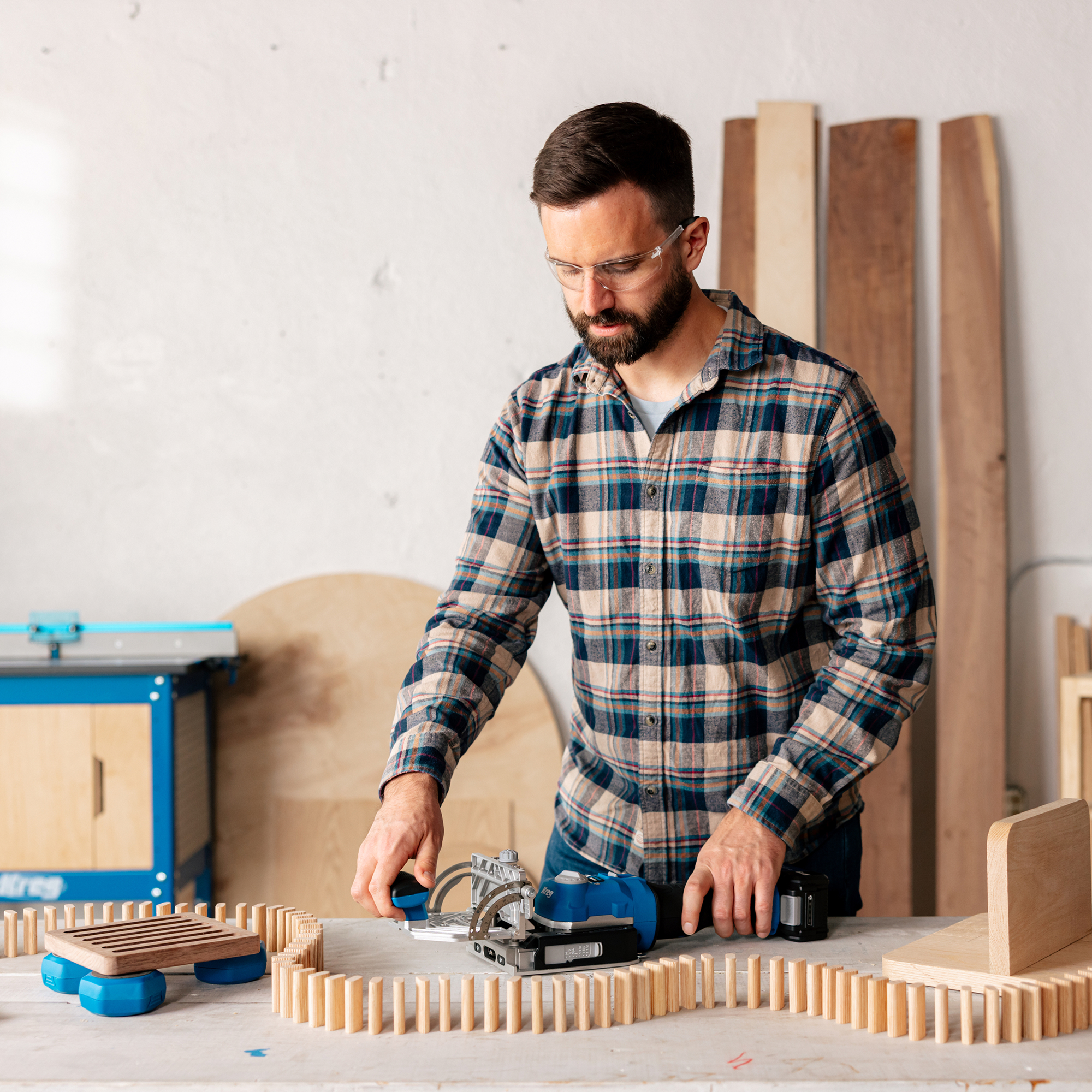 A man is adjusting his Kreg Edge loose tenon joiner while several tenons are set up as dominoes around him in his workshop