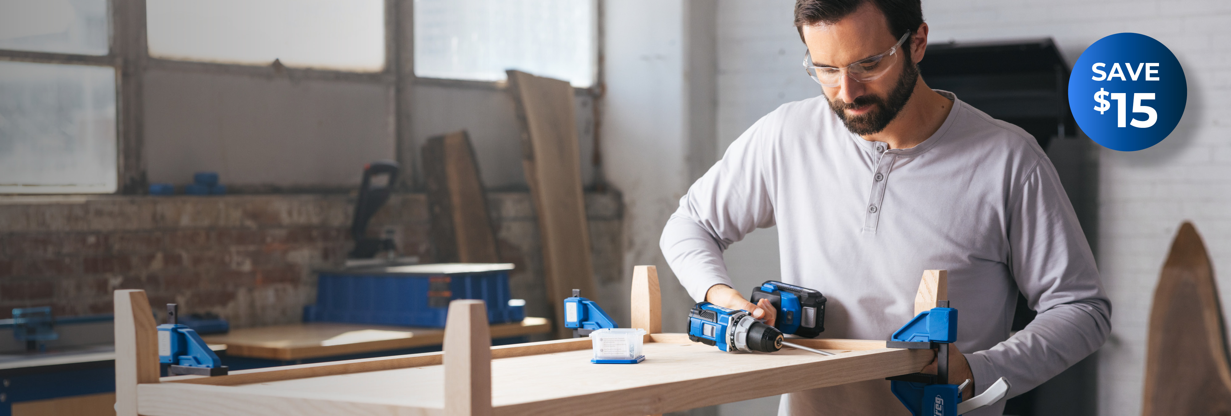 A man drills into a coffee table that he's building with a Kreg Ionic Drive drill. There is a blue burst on the image that says "Save $15."