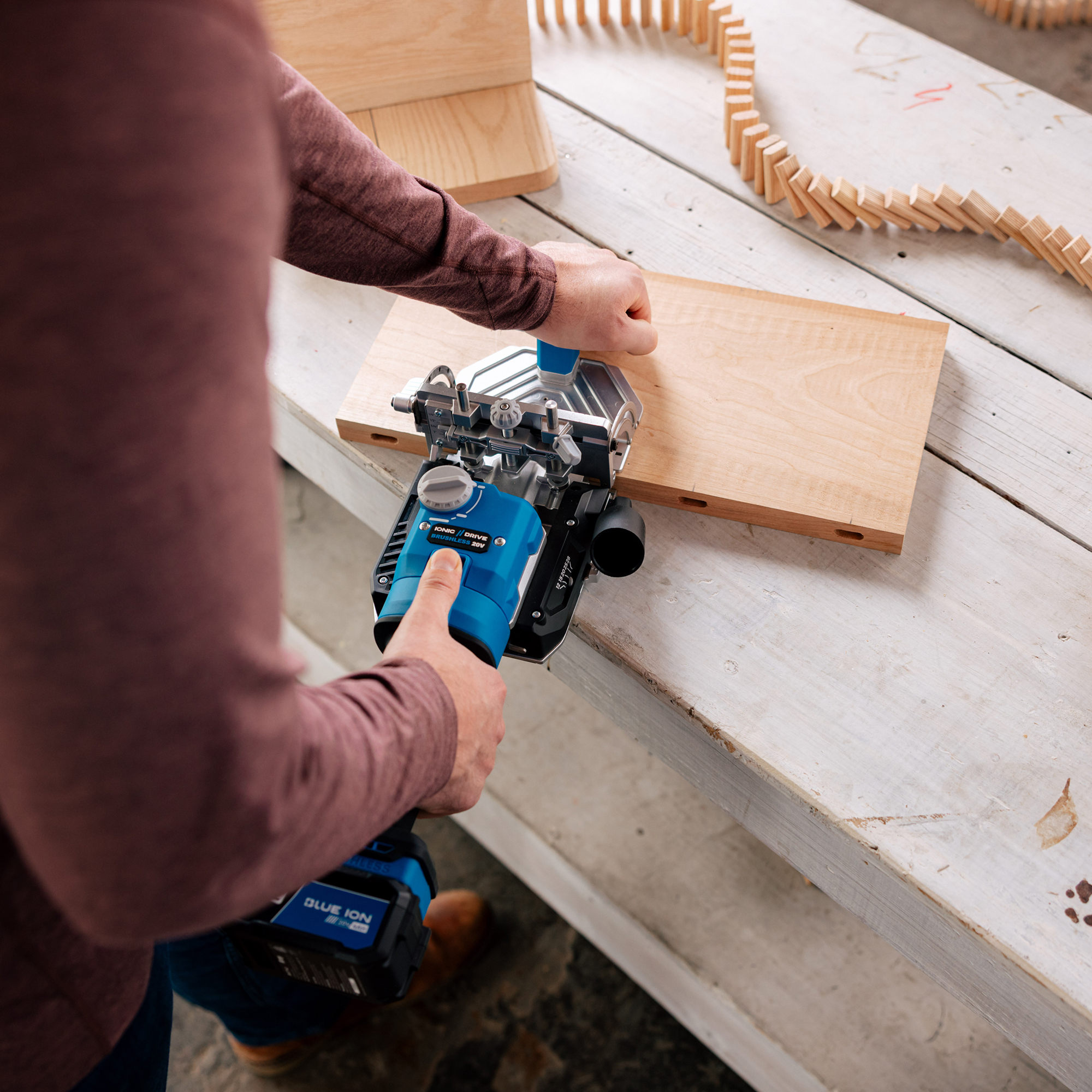 A man drills a mortise into a board with the Kreg Edge loose tenon joiner. Several wooden tenons are set up around the workspace as dominoes.