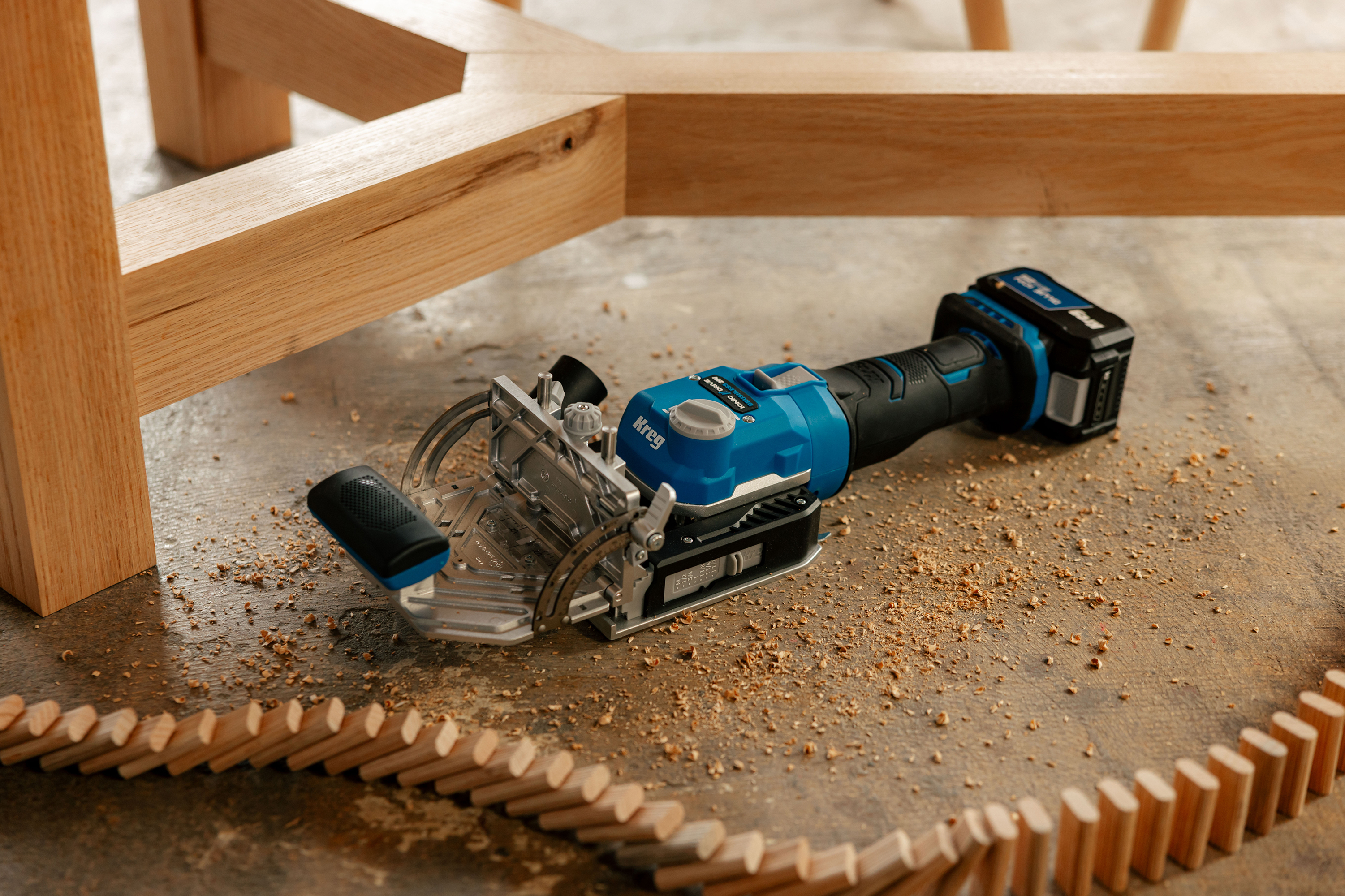 The Kreg Edge laying in a pile of sawdust under a table. Several tenons are set up as dominoes and are falling around it. 